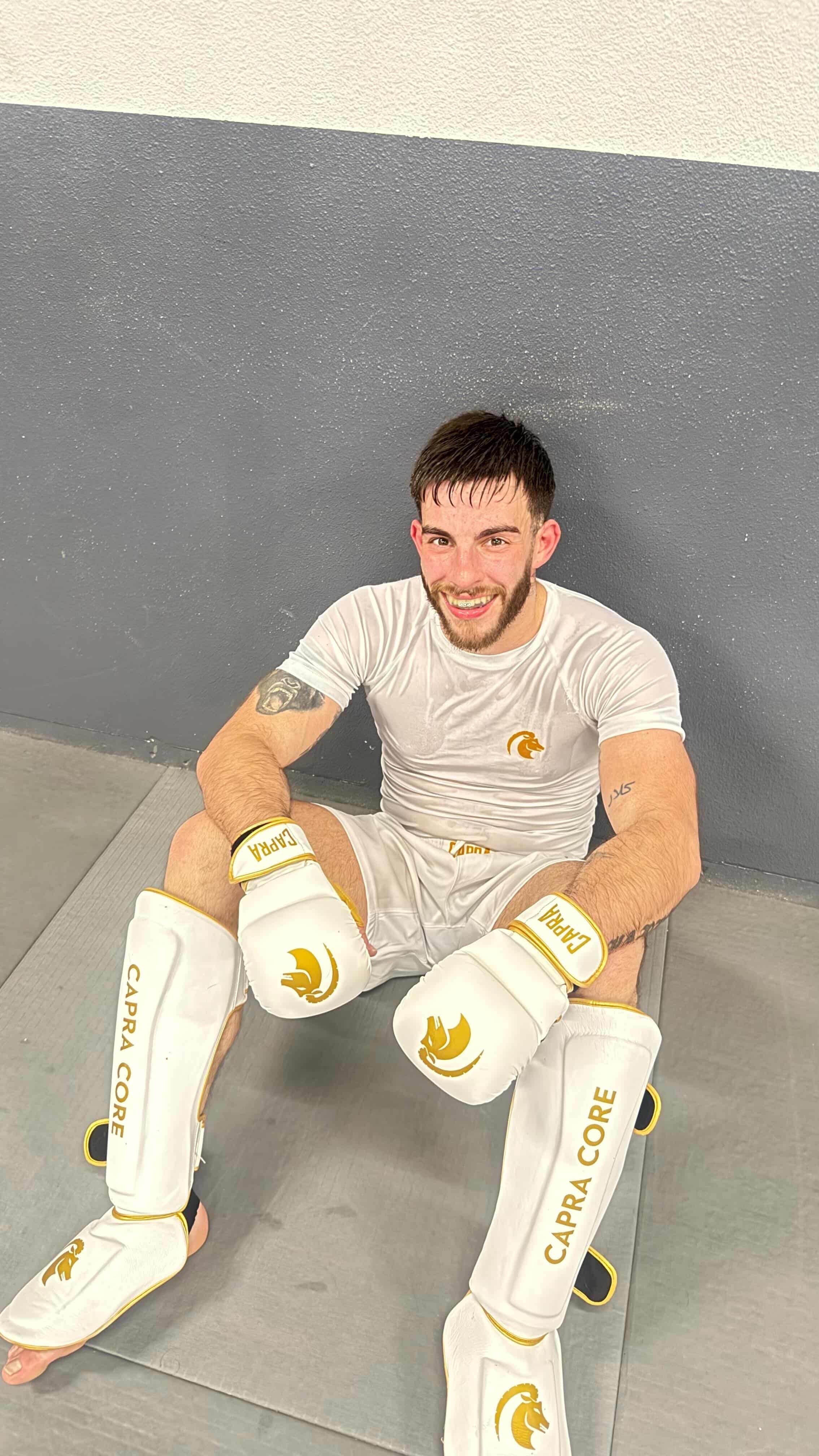 Jongen met Capra Core MMA-handschoenen, rashguard en short zittend voor training